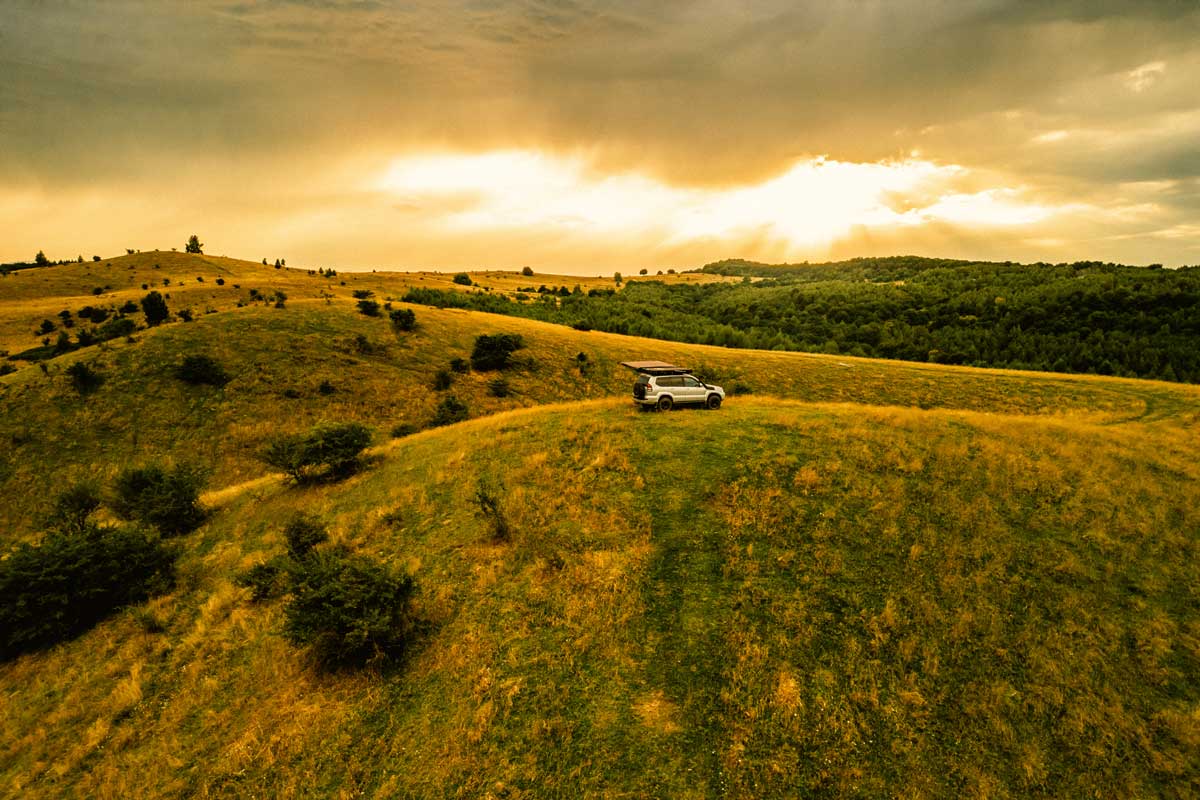 Camping on the hills beside a forest with a car awning and rooftop tent