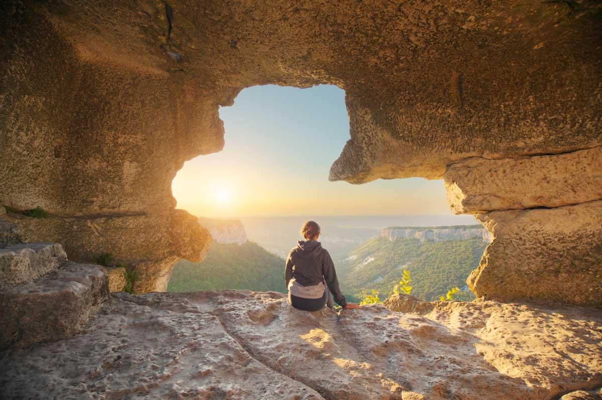 Woman looking out a mountain cave whilst overlanding
